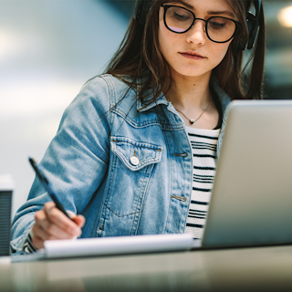 Online graduate student taking notes while attending an online course on their laptop